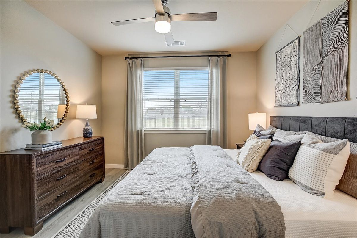 Secondary bedroom with gray upholstered headboard, dresser and mirror, and soft neutral bedding.